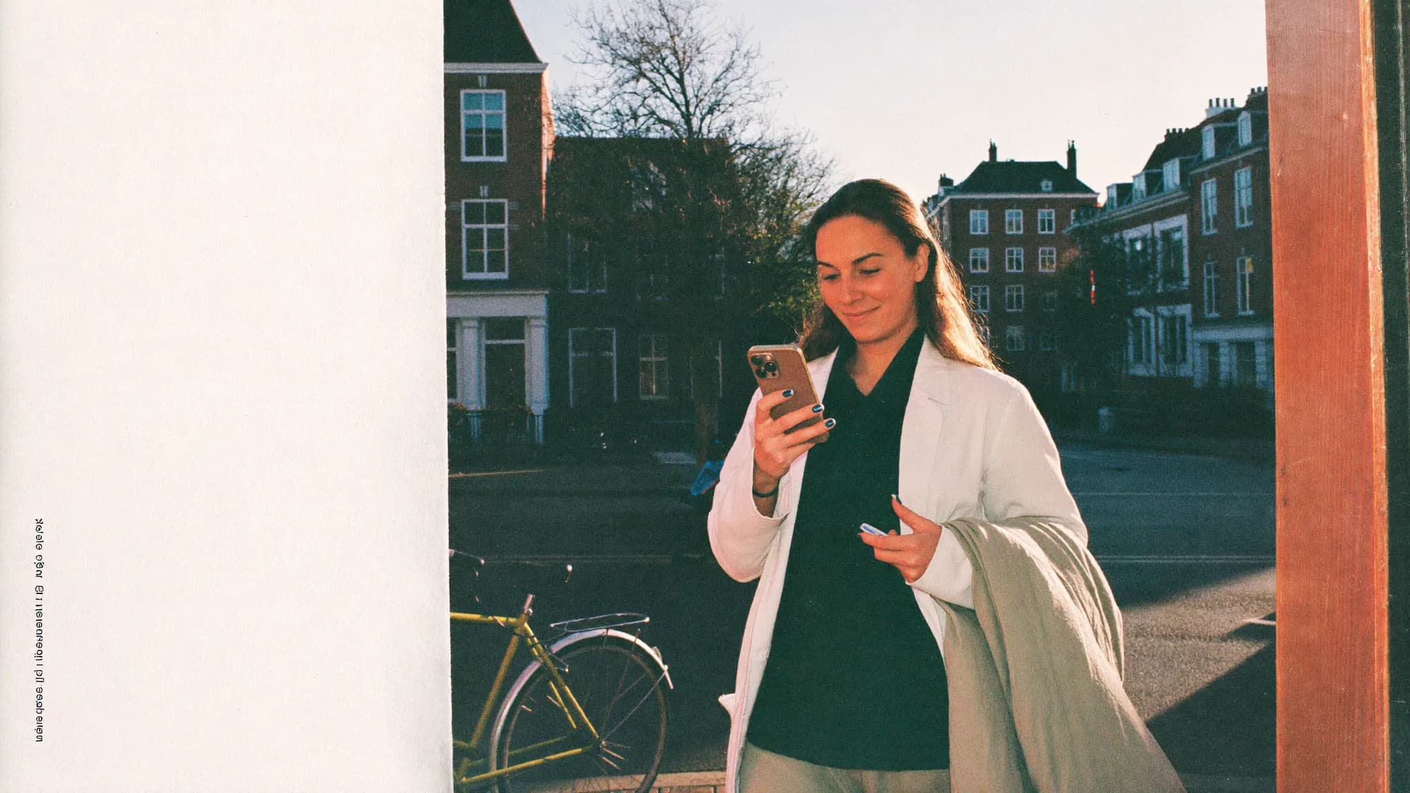Vrouw kijkt glimlachend op haar telefoon op straat, aan het eind van de middag