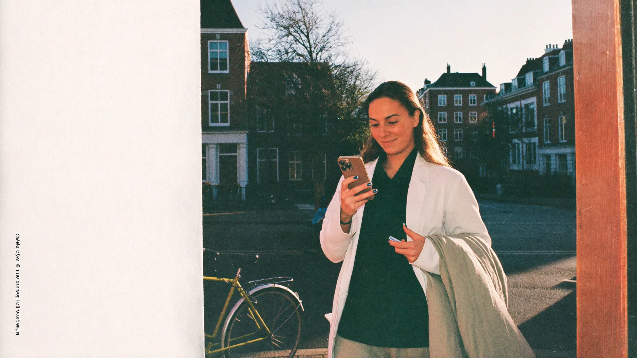 Een vrouw kijkt glimlachend op haar telefoon aan een gracht, aan het eind van de middag